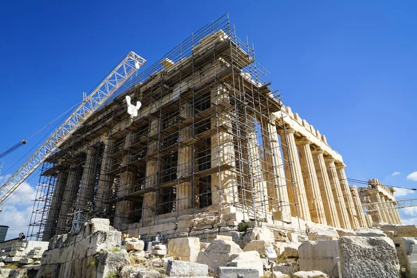 Restoration work in progress at world heritage classical Parthenon on marble block base on top of Acropolis with machine crane, scaffolding and blue sky background