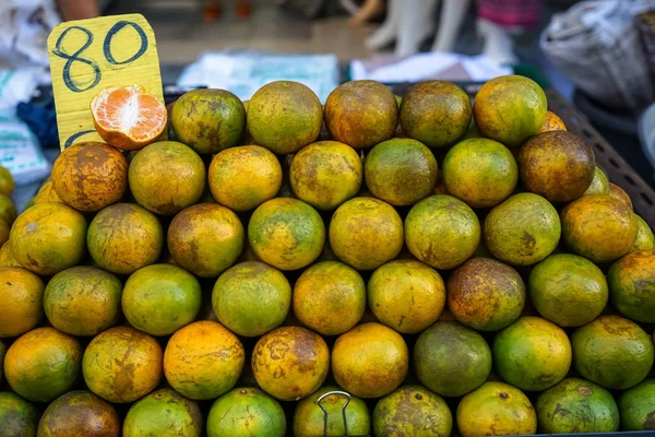 Pile of fresh organic local thai tangerine orange in yellow, green color and marked skin selling in market with price tag and half open fruit — Stock Photo, Image