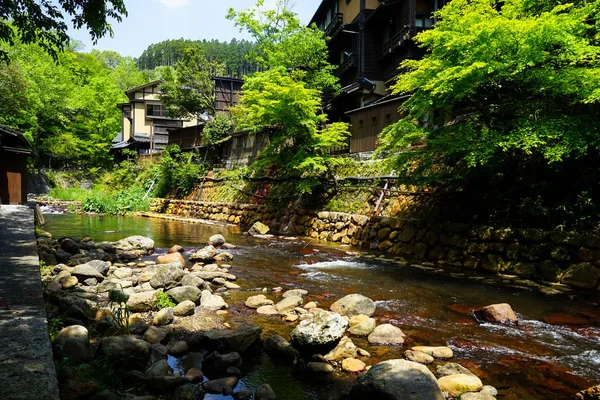 Weergave van verse rivier stream, stenen bank en natuurlijke rots strand met groene bomen en lokale gebouwen in Kurokawa onsen stad — Stockfoto