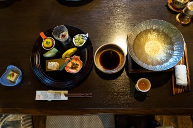 Japon ryokan kaiseki yemek meze ordövr tabakları, güveç hazırlık, soya sosu kase, içki Kupası, sofra ve sıcak havlu ahşap masa üzerinde de dahil olmak üzere
