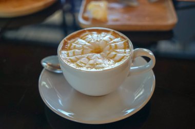 Caffe sütlü latte sanat tasarım örümcek web çiçek desen beyaz Kupası ve uçan daire sütlü köpük tabakası üzerinde siyah cam masa ve arka plan bulanık ışık yansıması ile