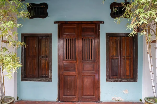 Casa de fileira fachada fundo mostrar escuro porta de entrada de madeira e janelas com haste de aço na parede azul claro com planta de bambu pote primeiro plano e piso de terracota — Fotografia de Stock