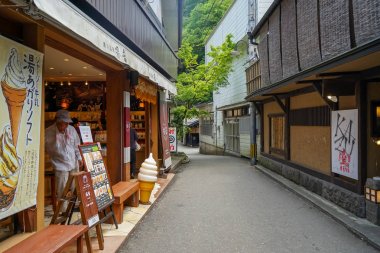 Local vintage street atmosphere with an unidentified man in ice cream shop and restaurant buildings, Kurokawa Onsen town clipart