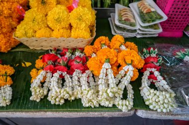 Fresh Thai style flower garlands made of white jasmine, crown flower, red rose and  yellow marigold with betel nut tray selling on green banana leaves in local market clipart