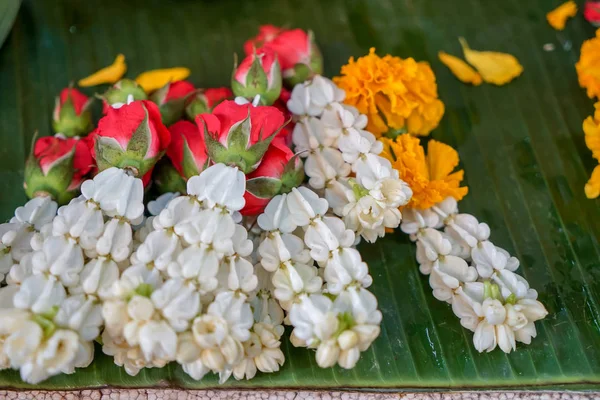 Fresh Thai style flower garlands made of white jasmine, crown flower, red rose and  yellow marigold selling on green banana leaves in local market, selective focus