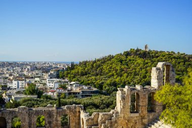 Atina cityscape ve lowrise beyaz binalar mimari, dağ, ağaçlar ve açık mavi gökyüzü arka plan görmek antik taş tiyatro ile Philopappu anıt görünümü