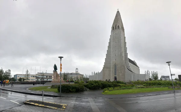 REYKJAVIK, ISLANDIA - 2 de julio de 2018: Hallgrimskirkja, una iglesia parroquial luterana con estatura de Leif Erikson y gente en el cielo nublado. Edificio catedral con fachada de hormigón . — Foto de Stock