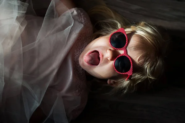 Ein kleines süßes kaukasisches Mädchen mit Sonnenbrille liegt auf dem Boden ein — Stockfoto