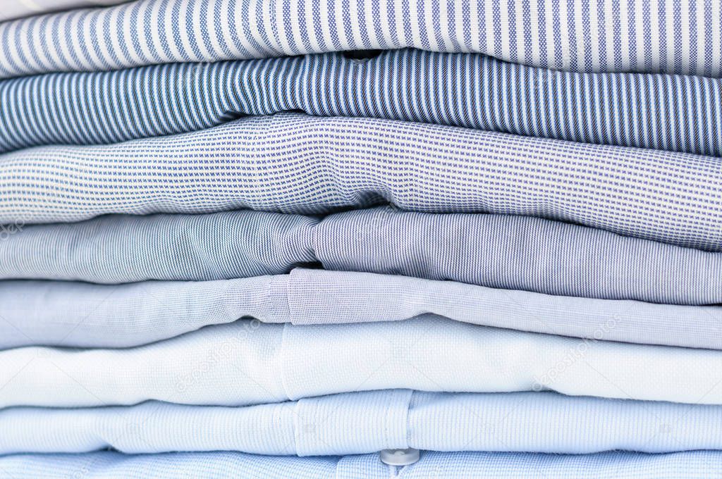 Neatly folded men's shirts of pastel tones.
