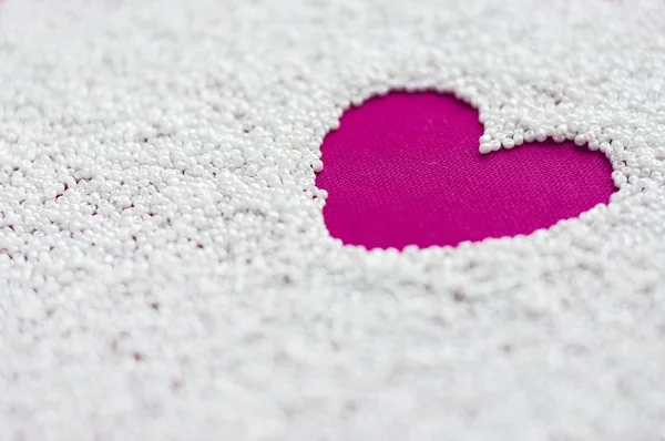 Corazón sobre un tejido de color rosa brillante en forma de un espacio de cuentas blancas. Primer plano con enfoque suave. Concepto de amor . — Foto de Stock