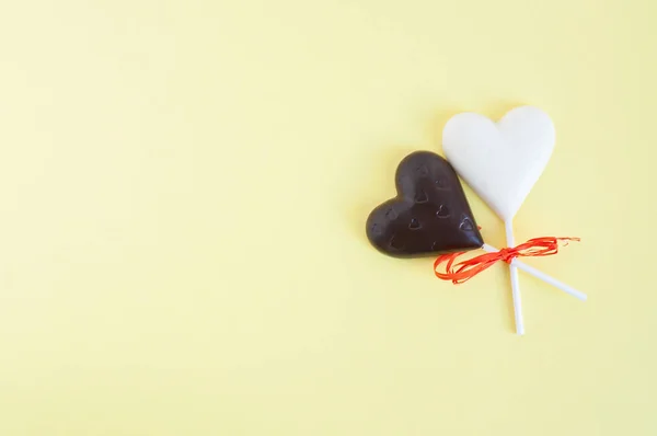 Doces de chocolate preto e branco na forma de um coração em um pau, enfaixado com uma fita laranja em um fundo amarelo claro. Cartão para o Dia dos Namorados . — Fotografia de Stock