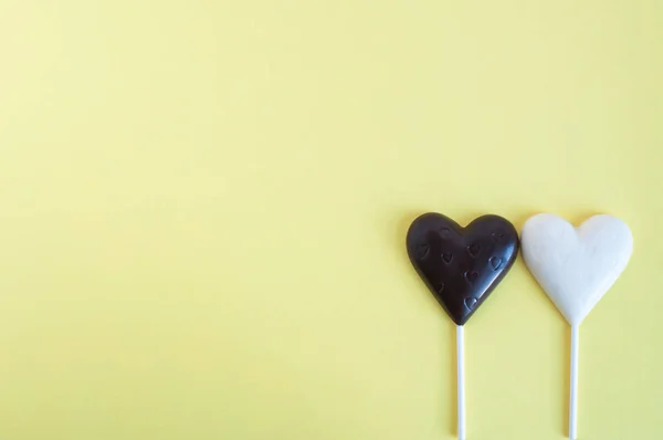Dulces de chocolate blanco y negro en forma de corazón sobre un palo sobre un fondo amarillo claro. Tarjeta para el Día de San Valentín . — Foto de Stock