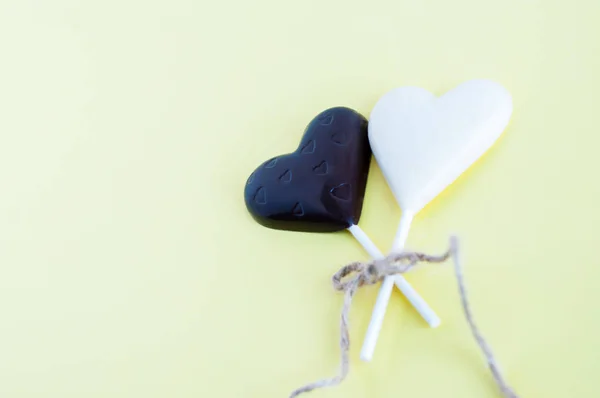 Doces de chocolate preto e branco na forma de um coração em um pau, amarrado com uma corda fina grossa em um fundo amarelo claro . — Fotografia de Stock