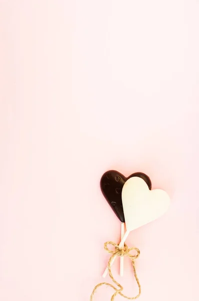 黑色和白色的巧克力糖果在一根棍子的心脏的形状, 用一根粗细的绳子栓在淡粉红色背景。情人节贺卡. — 图库照片
