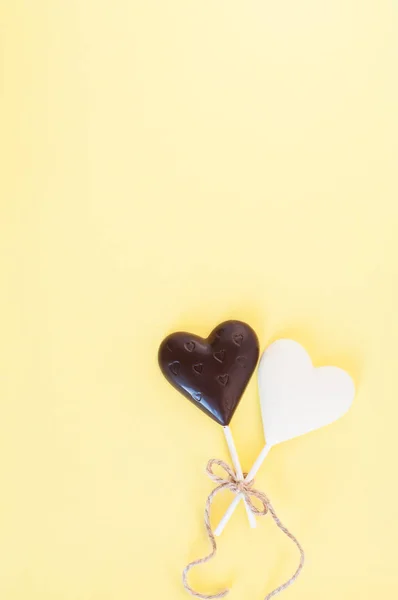 Dulces de chocolate blanco y negro en forma de corazón en un palo, atado con una cuerda gruesa y delgada sobre un fondo amarillo claro. Tarjeta para el Día de San Valentín . — Foto de Stock