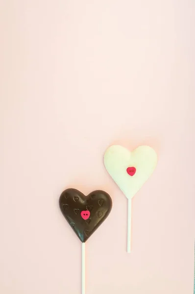 Bonbons au chocolat noir et blanc en forme de coeur sur un bâton sur un fond rose clair. Carte verticale jusqu'à la Saint-Valentin . — Photo