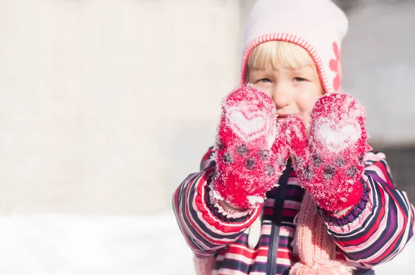 Μικρό κορίτσι με τα κόκκινα γάντια με λευκό καρδιά δείχνει τα χέρια το χειμώνα. Κινηματογράφηση σε πρώτο πλάνο τα χέρια στο επίκεντρο. Το φόντο είναι θολή απαλά Royalty Free Εικόνες Αρχείου