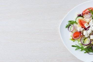 Salatalık, domates, peynir ve roka hafif ahşap arka plan üzerinde beyaz bir tabakta izole taze bahar salatası