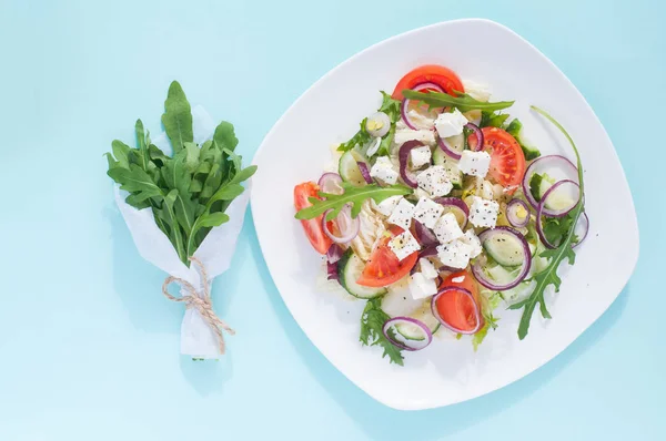 新鮮な春サラダ キュウリ トマト チーズ ルッコラの青色の背景に白いプレートに分離 — ストック写真