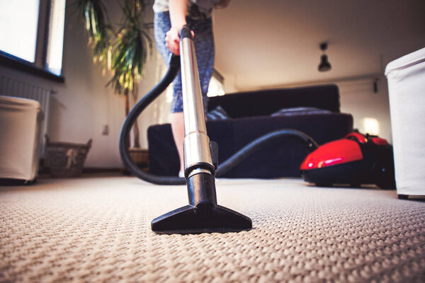 woman cleaning carpet with a vacuum cleaner in room - focus on h