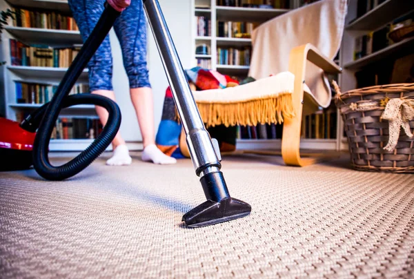 Woman cleaning carpet with a vacuum cleaner in room - focus on h — Stock Photo, Image