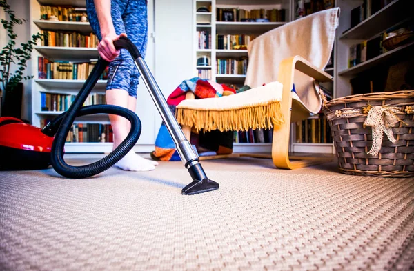 Woman cleaning carpet with a vacuum cleaner in room - focus on h — Stock Photo, Image