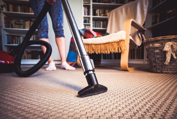 Woman cleaning carpet with a vacuum cleaner in room - focus on h — Stock Photo, Image