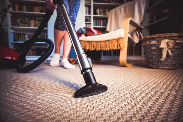 Woman cleaning carpet with a vacuum cleaner in room - focus on h — Stock Photo, Image