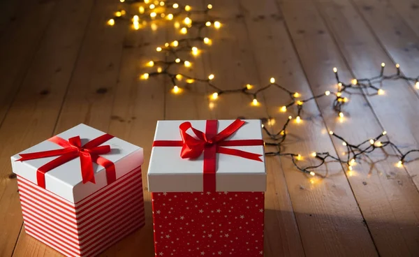 Rote Geschenkboxen und Weihnachtsbeleuchtung auf Holzboden — Stockfoto