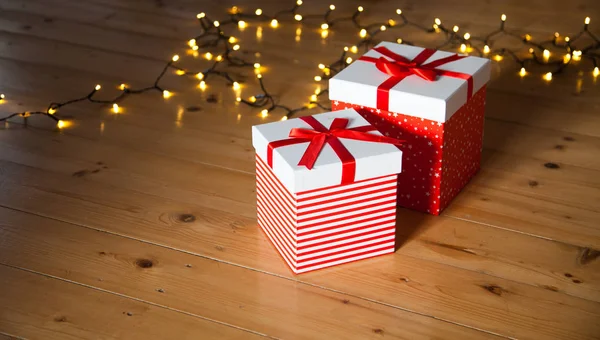 Rote Geschenkboxen und Weihnachtsbeleuchtung auf Holzboden — Stockfoto