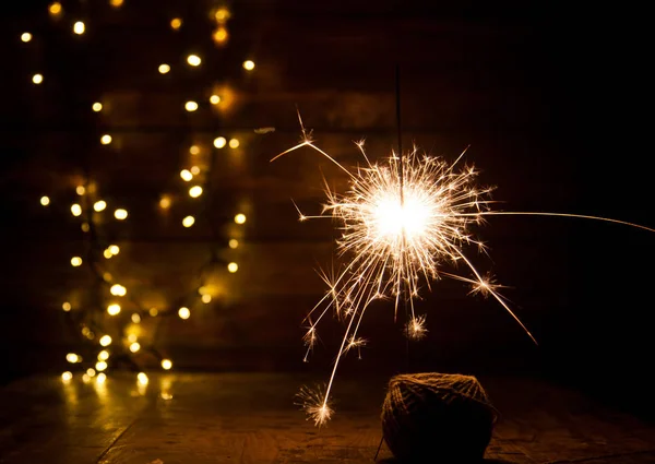Burning sparkler and christmas lights on wooden background — Stock Photo, Image