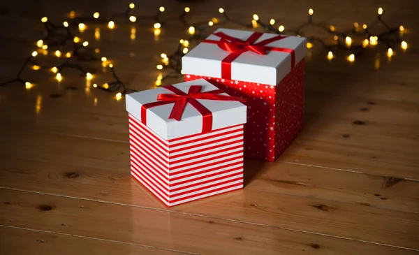Rote Geschenkboxen und Weihnachtsbeleuchtung auf Holzboden — Stockfoto