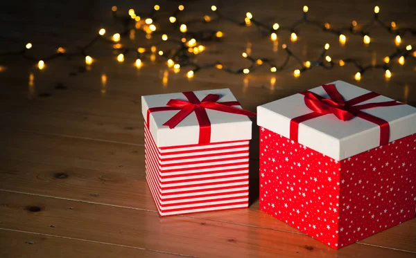 Rote Geschenkboxen und Weihnachtsbeleuchtung auf Holzboden — Stockfoto