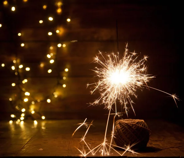 Burning sparkler and christmas lights on wooden background — Stock Photo, Image