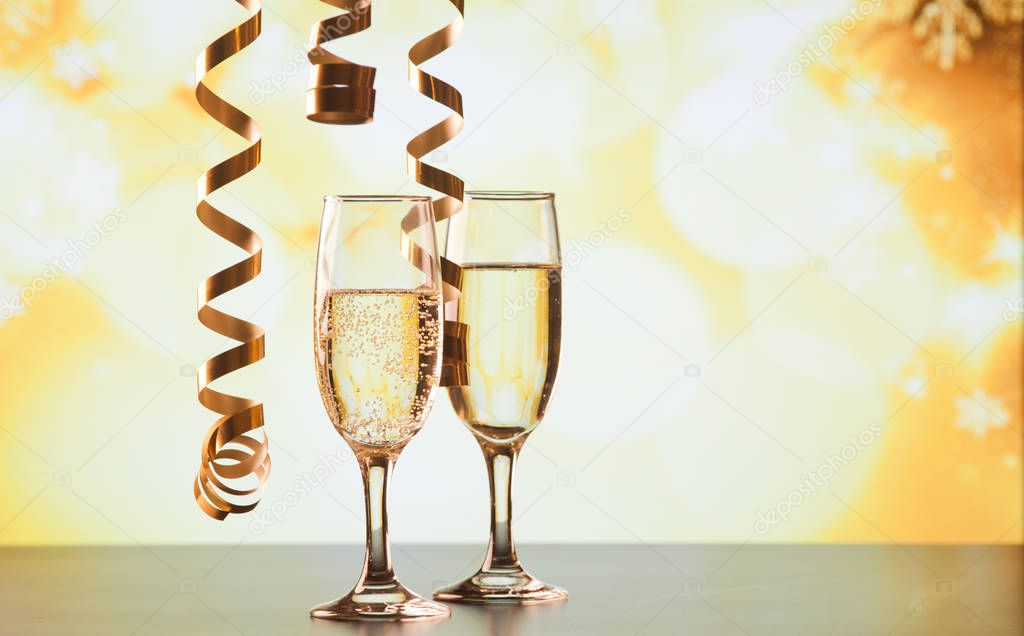 two champagne glasses with ribbons against holiday lights and fi