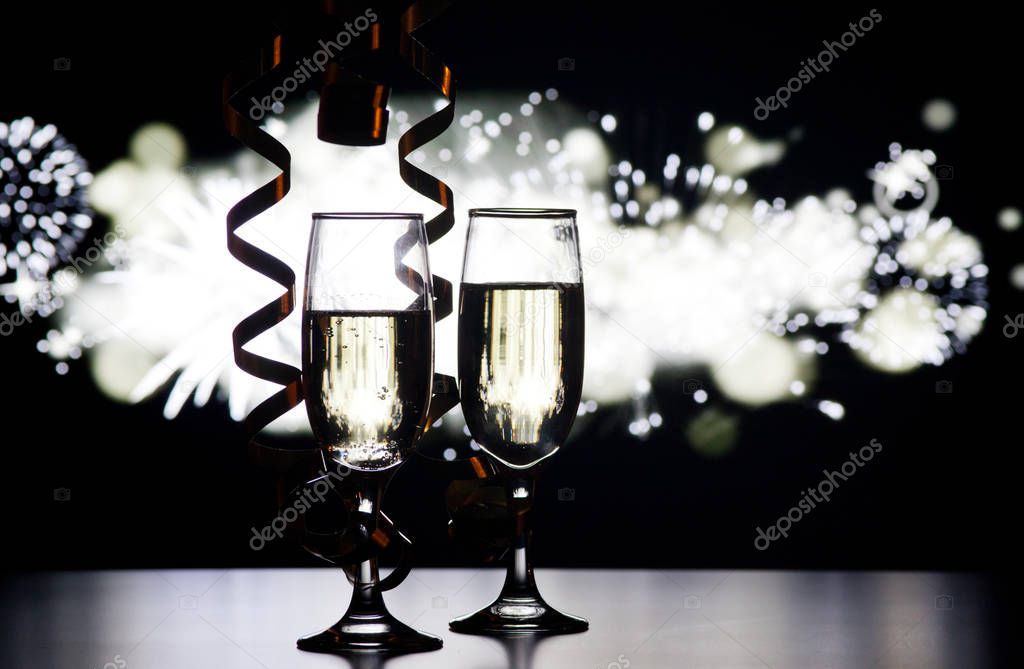 two champagne glasses with ribbons against holiday lights and fi