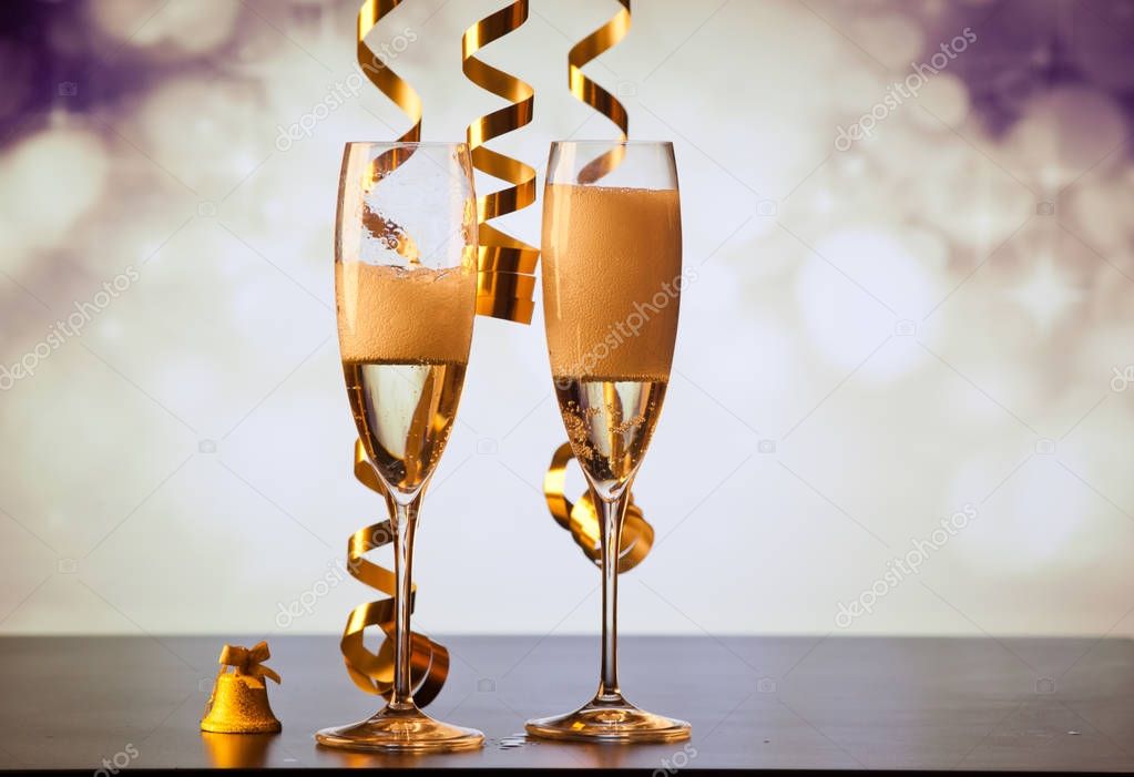 two champagne glasses with ribbons against holiday lights and fi
