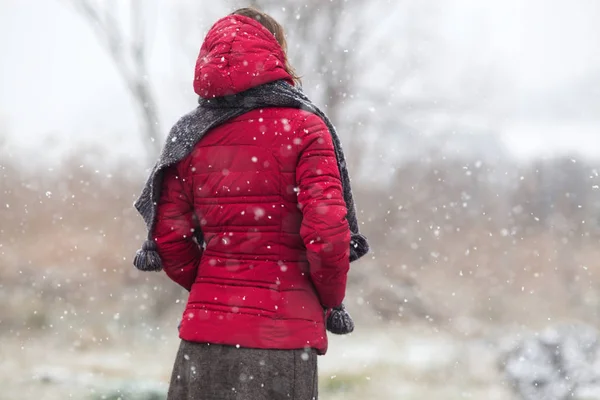 Mujer en abrigo rojo caminando en fuertes nevadas en el campo —  Fotos de Stock