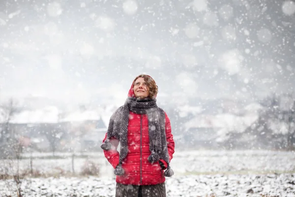 Mujer en abrigo rojo caminando en fuertes nevadas en el campo —  Fotos de Stock