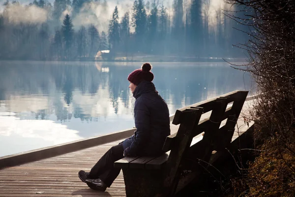 Gölün kenarında sisli bir sonbahar sabahı bankta oturan bir kadın. — Stok fotoğraf