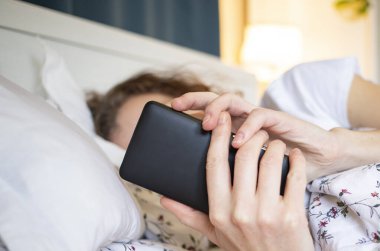 Yatakta akıllı telefon kullanan kadın.