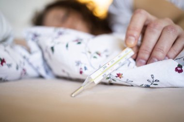 Ateşli bir kadın yatakta termometre koronavirüs ya da COVID-19 semptomlarına odaklanır.