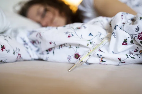 熱のあるベッドで女性は 温度計のコロナウイルスやCovid 19症状に焦点を当てます — ストック写真