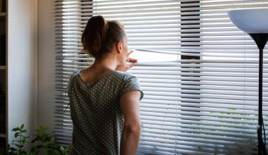 COVID-19 Karantina Akıl Sağlığı. Evde kendini izole etmiş bir kadın pencereden dışarı bakıp ilişki, istihdam ve koronavirüsü düşünüyor..