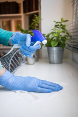 Yüzeyde ev temizliği antibakteriyel sprey sprey spreyi sıkarak COVID-19 'a karşı dezenfekte ederek mavi eldiven takarak yayılıyor. Hastanelerde ve kamusal alanlarda yüzeylerin temizlenmesi.