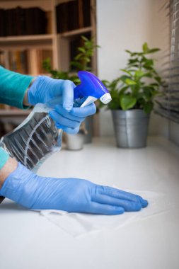 Yüzeyde ev temizliği antibakteriyel sprey sprey spreyi sıkarak COVID-19 'a karşı dezenfekte ederek mavi eldiven takarak yayılıyor. Hastanelerde ve kamusal alanlarda yüzeylerin temizlenmesi.