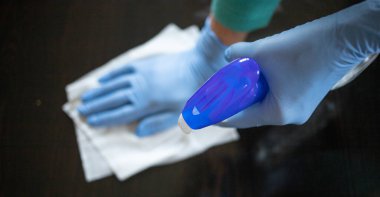 Yüzeyde ev temizliği antibakteriyel sprey sprey spreyi sıkarak COVID-19 'a karşı dezenfekte ederek mavi eldiven takarak yayılıyor. Hastanelerde ve kamusal alanlarda yüzeylerin temizlenmesi.