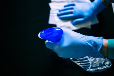 Yüzeyde ev temizliği antibakteriyel sprey sprey spreyi sıkarak COVID-19 'a karşı dezenfekte ederek mavi eldiven takarak yayılıyor. Hastanelerde ve kamusal alanlarda yüzeylerin temizlenmesi.