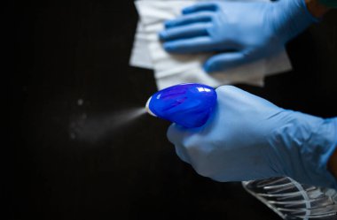 Yüzeyde ev temizliği antibakteriyel sprey sprey spreyi sıkarak COVID-19 'a karşı dezenfekte ederek mavi eldiven takarak yayılıyor. Hastanelerde ve kamusal alanlarda yüzeylerin temizlenmesi.