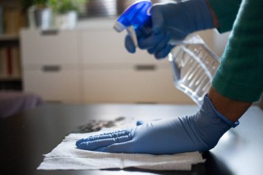 Yüzeyde ev temizliği antibakteriyel sprey sprey spreyi sıkarak COVID-19 'a karşı dezenfekte ederek mavi eldiven takarak yayılıyor. Hastanelerde ve kamusal alanlarda yüzeylerin temizlenmesi.